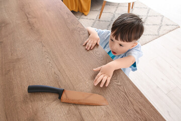 Naklejka premium Little boy trying to take knife from high table in kitchen, top view. Child at risk