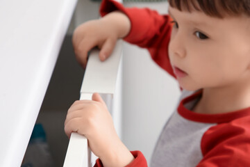Little boy opening drawer in kitchen, closeup. Child at risk
