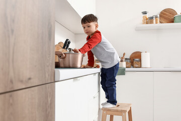 Little boy with cooking pot on stove in kitchen. Child at risk