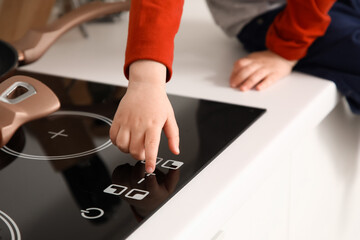 Little boy turning on electric stove in kitchen, closeup. Child at risk