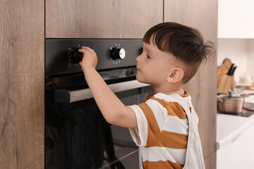 Little boy turning on oven in kitchen. Child at risk