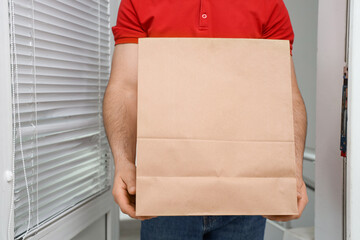 Male courier with paper bag at doorway. Food delivery service