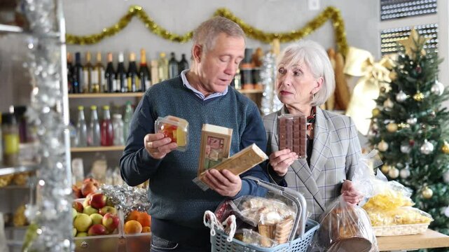 Preparing for Christmas celebration - elderly husband and wife buying nougat, panettone and chocolate in supermarket. High quality 4k footage
