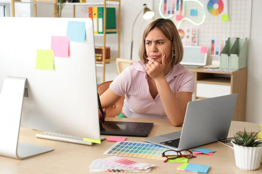 Thoughtful female web designer working with graphic tablet at table in office - Powered by Adobe