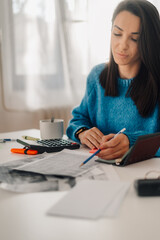 Accountant calculating tax using calculator and taking notes at home office desk