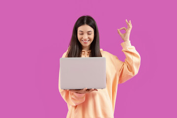 Young woman with laptop showing OK on violet background