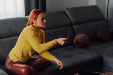 Woman using remote control while watching tv on sofa at home