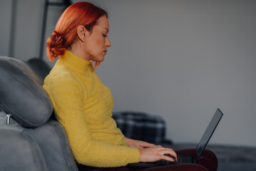 Focused woman working remotely from home using laptop on sofa
