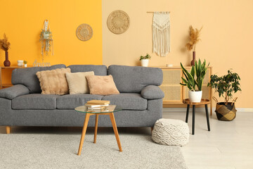 Comfortable grey sofa, pouf and table in interior of light living room