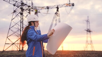 An electrician on the background of high towers of power plants looks at the project for the development of an electrical structure, the expansion of the electrical voltage of volts in the wires.