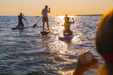 young people  riding  on sup surfing in the sea at sunset.