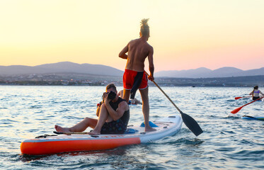 young mens  riding  on sup surfing in the sea at sunset