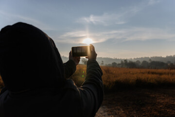 person is seen holding a smartphone, capturing a sunrise or sunset in a wide field.
