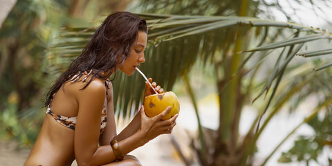 Exotic Bikini Model Sips Coconut on Sandy Beach Surrounded by Palms