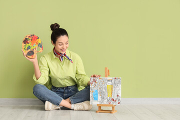 Young woman with palette and painting by numbers sitting near green wall