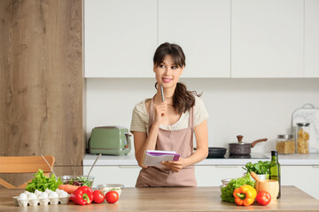 Thoughtful young woman writing recipe in book at home