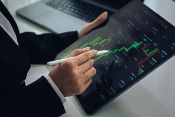 An investor monitors real-time stock market data on a smartphone and laptop, analyzing charts,...