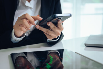 An investor monitors real-time stock market data on a smartphone and laptop, analyzing charts,...