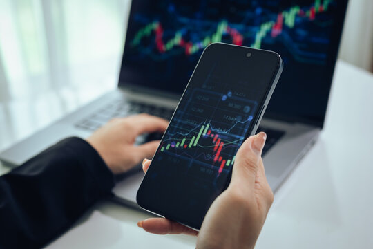 An investor monitors real-time stock market data on a smartphone and laptop, analyzing charts, financial trends, and cryptocurrency for informed trading decisions in a digital workspace.