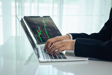An investor monitors real-time stock market data on a smartphone and laptop, analyzing charts,...