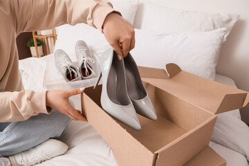 Woman putting high heels into shoe box in bedroom
