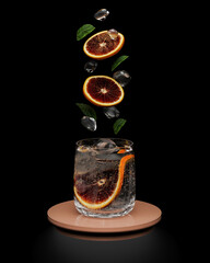 Fruit slices, mint and ice falling in glass with drink on black background, cocktail concept, 3d...