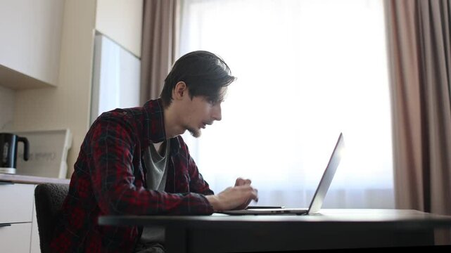 a young man of 23 concentrate our energy and using a laptop, connecting to the Internet in the kitchen at home. Working from. Study online. work from vacation home, remote workers. 