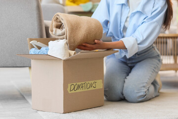 Young woman packing sweater into box for donation at home