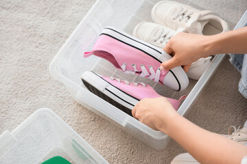 Young woman keeping her sneakers in container at home, closeup