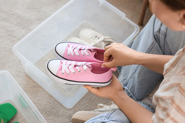 Young woman putting sneakers into container at home, closeup