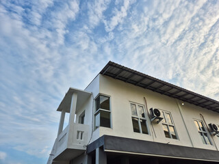 Modern two-story white building with air conditioners and balcony under a cloudy blue sky