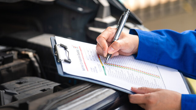 Action of a repairman is checking on multi-point checklist form during perform service the car parts. Industrial working scene, close-up and selective focus.