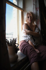 Obraz premium Beautiful girl artist posing on the windowsill of an art studio background.