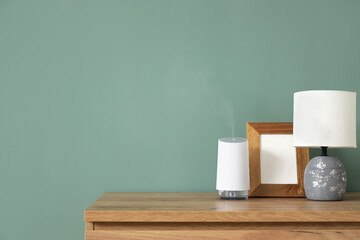 Air humidifier with blank frame and lamp on shelf near green wall