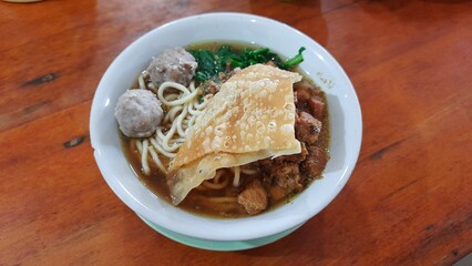 A Delicious Bowl of Mie Ayam on wood table. Indonesian Chicken Noodle Soup