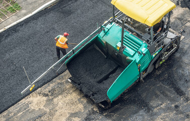 Workers lay a new asphalt coating using hot bitumen. Work of heavy machinery and paver. Top view