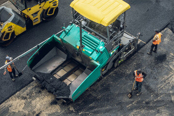 Workers lay a new asphalt coating using hot bitumen. Work of heavy machinery and paver. Top view