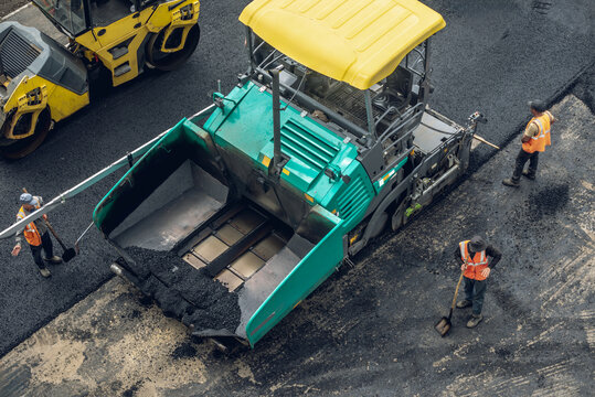 Workers lay a new asphalt coating using hot bitumen. Work of heavy machinery and paver. Top view