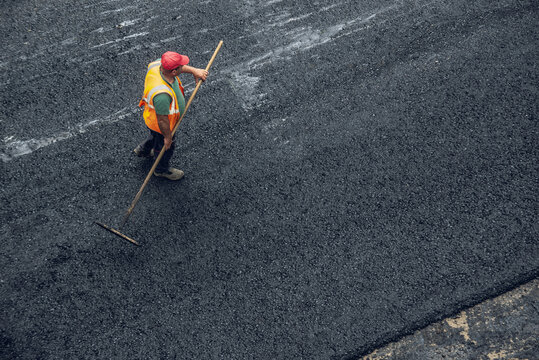 Workers lay a new asphalt coating using hot bitumen. Work of heavy machinery and paver. Top view