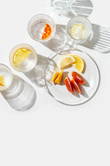 Crystal glasses with citrus slices in water on white background with rainbow reflections at...