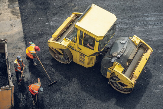 Workers lay a new asphalt coating using hot bitumen. Work of heavy machinery and paver. Top view
