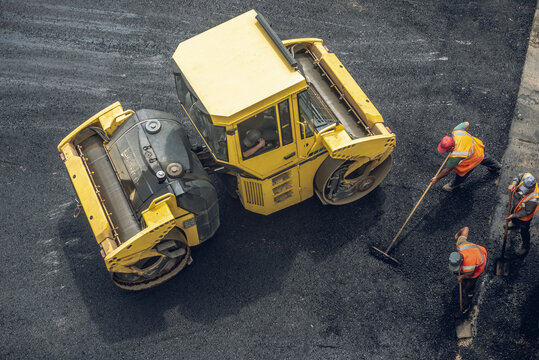 Workers lay a new asphalt coating using hot bitumen. Work of heavy machinery and paver. Top view
