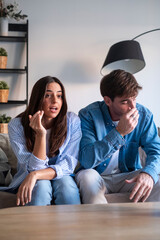 Couple sitting on a sofa during a serious conversation, expressing tension and concern. A...
