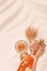 Glasses of rose wine on pink background with palm leaf shadows from sunlight. Minimal Top view...