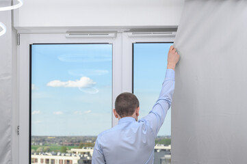 Man covers heavy grey curtain at home, protect privacy, hide