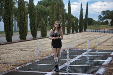 Young, beautiful, blonde woman wearing a black top and skirt, with boots, looking sweetly,...