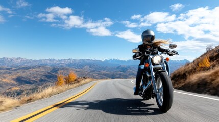 Fototapeta premium A dynamic shot capturing a confident female rider on a motorcycle speeding along a winding road, framed by breathtaking mountains under a brilliant blue sky.