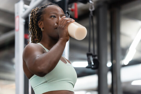 Young female athlete drinking protein shake after workout in gym