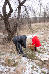 Bonding moments in winter woods as a child in a red coat plays with a cat while an adult crouches nearby on a chilly day