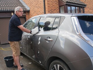 Man washing a silver car with a hand glove in a driveway at home